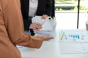 secretary searches through stacked paperwork on desk in office to find lease within stacked paperwork just before meeting. concept difficulty in finding hire purchase contract from stacked paperwork photo