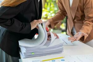 secretary searches through stacked paperwork on desk in office to find lease within stacked paperwork just before meeting. concept difficulty in finding hire purchase contract from stacked paperwork photo