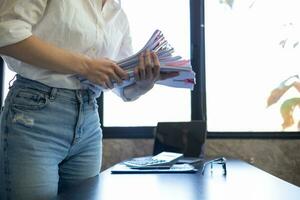 secretary searches through stacked paperwork on desk in office to find lease within stacked paperwork just before meeting. concept difficulty in finding hire purchase contract from stacked paperwork photo