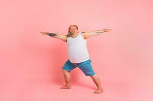 Funny man with beard in yoga position on studio pink background photo