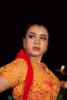 Javanese woman in a traditional orange dress while wearing makeup and a red scarf at a dance festival photo