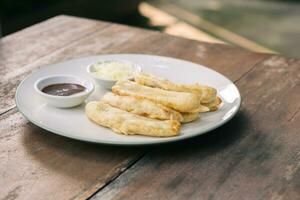 Tasty deep fried banana slices on wooden table with chocolate sauce. Popular street food in South East Asia photo