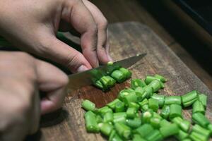 Photo of female hand chopping green beans on wooden cutting board for cooking