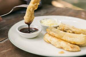 Tasty deep fried banana slices on wooden table with chocolate sauce and hand with fork photo