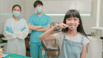 Portrait of Asian little girl with toothbrush for teeth brushes with female dentist and assistant, professional healthcare work in kid hospital, happy smile, and looking at camera in dental clinic. video