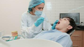 asiatisk kvinna tandläkare undersöka ung manlig patient tänder och tandvärk stomatologi i dental klinik, välbefinnande hygien checkar, och professionell ortodontisk sjukvård arbete i läkares kontor sjukhus. video