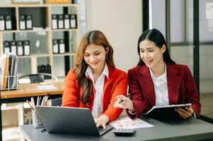 Two Asian businesswoman discuss investment project working and planning strategy with tablet laptop computer in office. photo