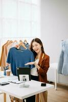 Fashion blogger concept, Young Asian women selling clothes on video streaming.Startup small business SME, using smartphone or tablet taking receive and checking photo