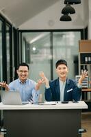 Two Asian business workers talking on the smartphone, tablet and using laptop at the office. photo