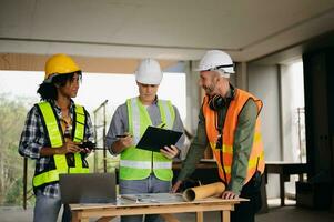 Contractor and architect looking at plan, tablet, laptop and talking about working on big project. Building in construction process interior. team work photo