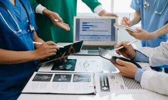 Medical team having a meeting with doctors in white lab coats and surgical scrubs seated at a table discussing a patients working online using computers in medical industry photo