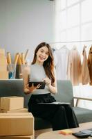 Fashion blogger concept, Young Asian women selling clothes on video streaming.Startup small business SME, using smartphone or tablet taking receive and checking photo