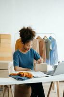 Young African woman running online store Startup small business SME, using smartphone or tablet taking receive and checking online purchase shopping order in office photo