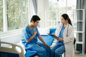 asiático masculino paciente en cama mientras médico manos de comprobación examinando su legumbres para grabar el tratamiento resultados en hospital foto