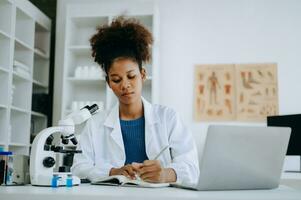 African smiling doctor or consultant sitting at a desk his neck writing sick note, surgery planning and prescription.and clinical report test results in office photo