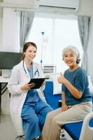 Friendly Female Head Nurse Making Rounds does Checkup on Patient Resting in Bed. She Checks tablet while Man Fully Recovering after Successful Surgery in hospital photo