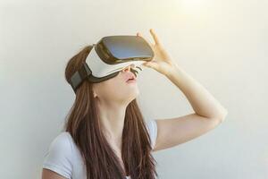 Smile young woman wearing using virtual reality VR glasses helmet headset on white background. Smartphone using with virtual reality goggles. Technology, simulation, hi-tech, videogame concept. photo