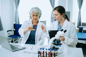 Two scientist or medical technician working, having a medical discuss meeting with an Asian senior female scientist supervisor in the laboratory with online reading, test samples and innovation photo