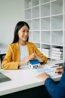 Female real estate agent is use hands to protect red roof for the concept of real estate investment about house trading, purchase at desk in office photo