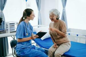 simpático hembra cabeza enfermero haciendo rondas lo hace chequeo en paciente descansando en cama. ella cheques tableta mientras hombre completamente recuperación después exitoso cirugía en hospital foto