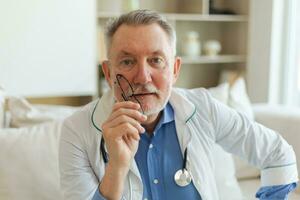 Mature senior male doctor in glasses medical uniform smiling looking at camera in hospital. General practitioner GP therapist professional healthcare expert in clinic. Healthcare concept. photo