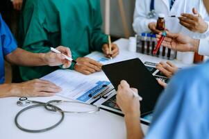 Medical team having a meeting with doctors in white lab coats and surgical scrubs seated at a table discussing a patients working online using computers photo