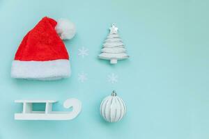 Simply minimal composition winter objects ornament Santa hat sled fir tree ball isolated on blue pastel trendy background photo