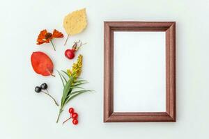 Autumn floral composition. Vertical frame mockup chokeberry rowan berries colorful leaves dogrose flowers on white background. Fall natural plants ecology concept. Flat lay top view, copy space photo