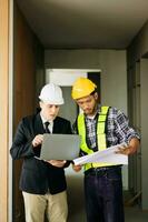 Contractor and architect looking at plan, tablet, laptop and talking about working on big project. Building in construction process photo