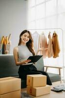 Fashion blogger concept, Young Asian women selling clothes on video streaming.Startup small business SME, using smartphone or tablet taking receive and checking photo