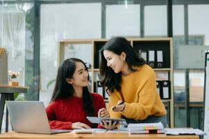 Two Attractive young Asian female college students working on the school project using laptop computer and tablet together, enjoy talking photo