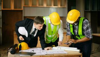 Contractor and architect looking at plan, tablet, laptop and talking about working on big project. Building in construction process photo