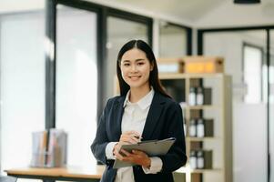 Confident business expert attractive smiling young woman holding digital tablet  on desk in office. photo
