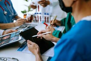 Medical team having a meeting with doctors in white lab coats and surgical scrubs seated at a table discussing a patients working online using computers photo