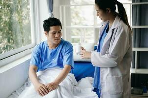 Doctor and young male patient who lie on the bed while checking pulse, consult and explain with nurse taking note in hospital photo