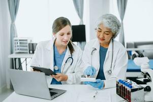 Medical team having a meeting with doctors in white lab coats and surgical scrubs seated at a table discussing a patients working online using computers in the medical industry photo