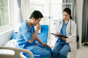 Asian doctor in white suit take notes while discussing and Asian elderly, man patient who lying on bed with receiving saline solution in hospital or clinic photo