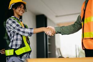 Construction team shake hands greeting start new project plan behind yellow helmet on desk in office center to consults about their building project. photo