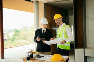Contractor and architect looking at plan, tablet, laptop and talking about working on big project. Building in construction process photo