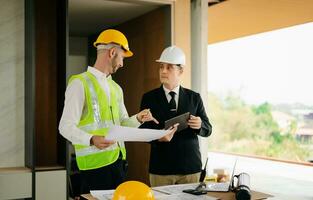 Contractor and architect looking at plan, tablet, laptop and talking about working on big project. Building in construction process photo