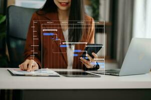 gerente de proyecto trabajando y actualizando tareas con hitos de planificación de progreso y diagrama de programación de diagramas de gantt. negocios que trabajan con teléfonos inteligentes, tabletas y computadoras portátiles en la oficina. foto