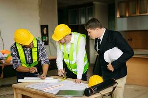 Contractor and architect looking at plan, tablet, laptop and talking about working on big project. Building in construction process photo