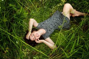 Brunette woman lying on green grass. Beauty Girl Outdoors enjoying nature and relaxation. Free Happy Woman, Top view photo