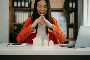 Asian Female real estate agent is use hands to protect red roof for the concept of real estate investment about house trading, purchase at desk in office photo