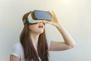 Smile young woman wearing using virtual reality VR glasses helmet headset on white background. Smartphone using with virtual reality goggles. Technology, simulation, hi-tech, videogame concept. photo