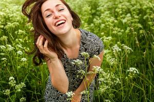 Beauty Girl Outdoors enjoying nature. Beautiful woman jumping on summer Field with blooming wild flowers, Sun Light. Free Happy Woman. photo