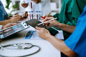 Medical team having a meeting with doctors in white lab coats and surgical scrubs seated at a table discussing a patients working online using computers photo