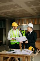 Contractor and architect looking at plan, tablet, laptop and talking about working on big project. Building in construction interior. photo
