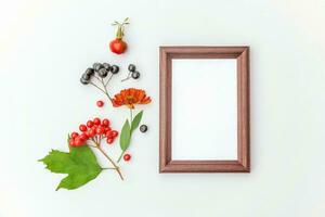 Autumn floral composition. Vertical frame mockup chokeberry rowan berries colorful leaves dogrose flowers on white background. Fall natural plants ecology concept. Flat lay top view, copy space photo