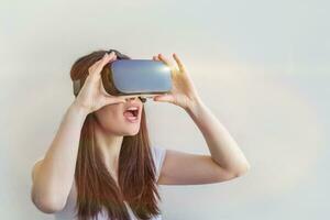 Smile young woman wearing using virtual reality VR glasses helmet headset on white background. Smartphone using with virtual reality goggles. Technology, simulation, hi-tech, videogame concept. photo